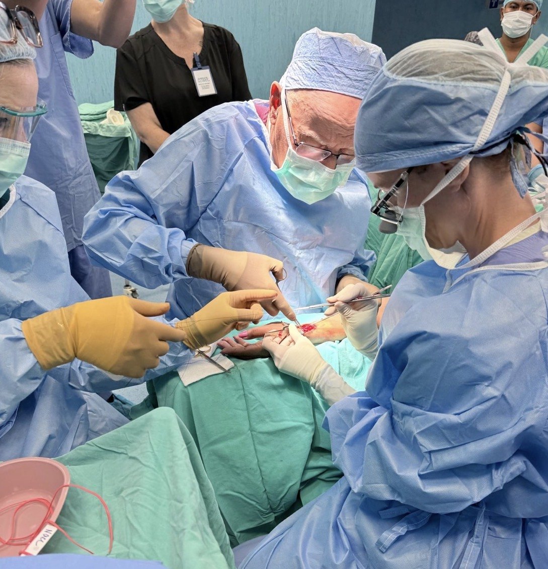 A man and a woman in scrubs and loupes operating on a draped arm