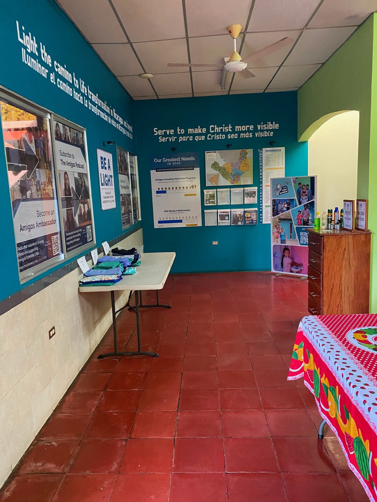 Amigos for Christ hub room with folded scrubs on a table and bilingual mission posters