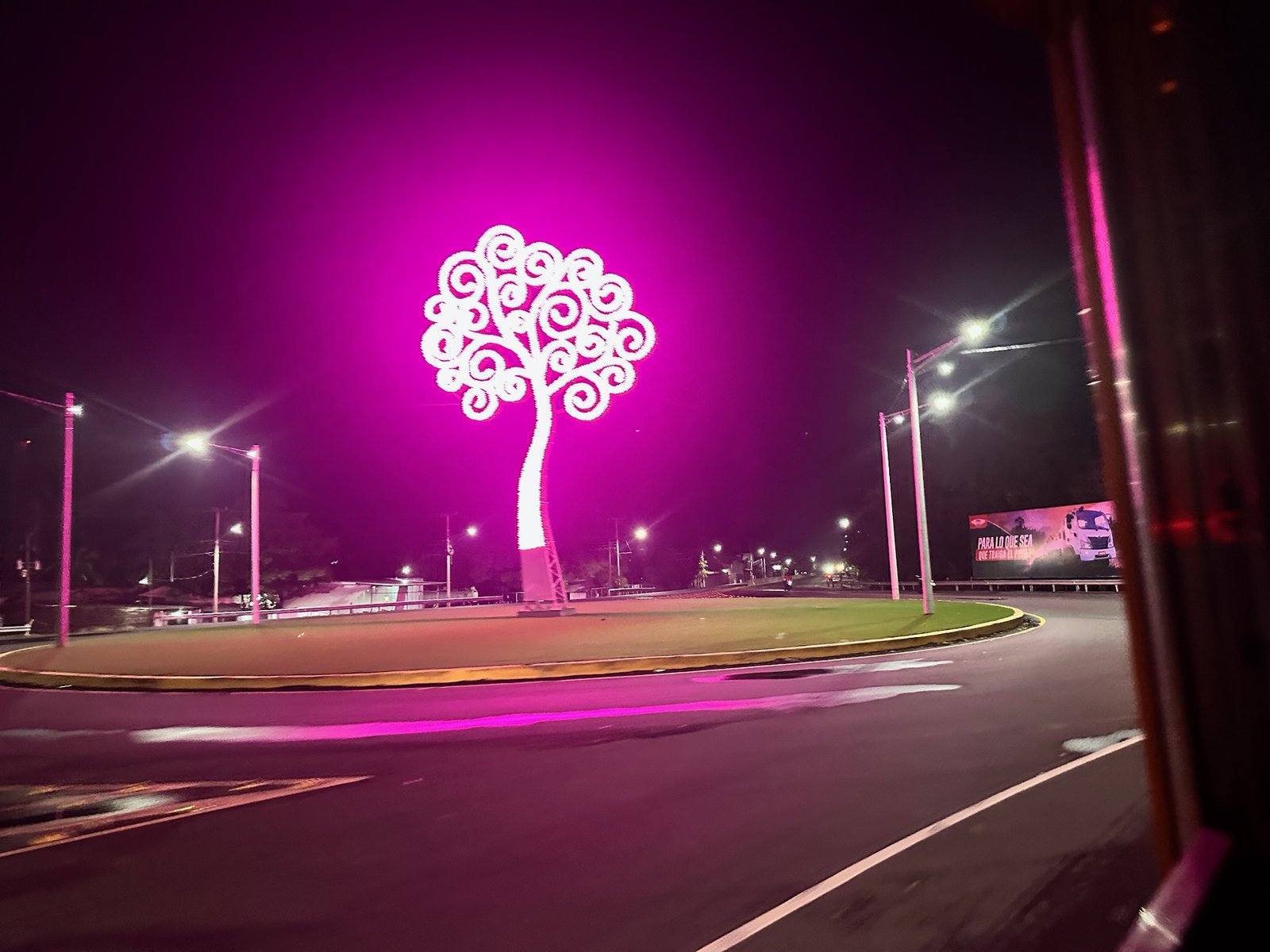 Magenta illuminated Tree of Life sculpture in a night roundabout