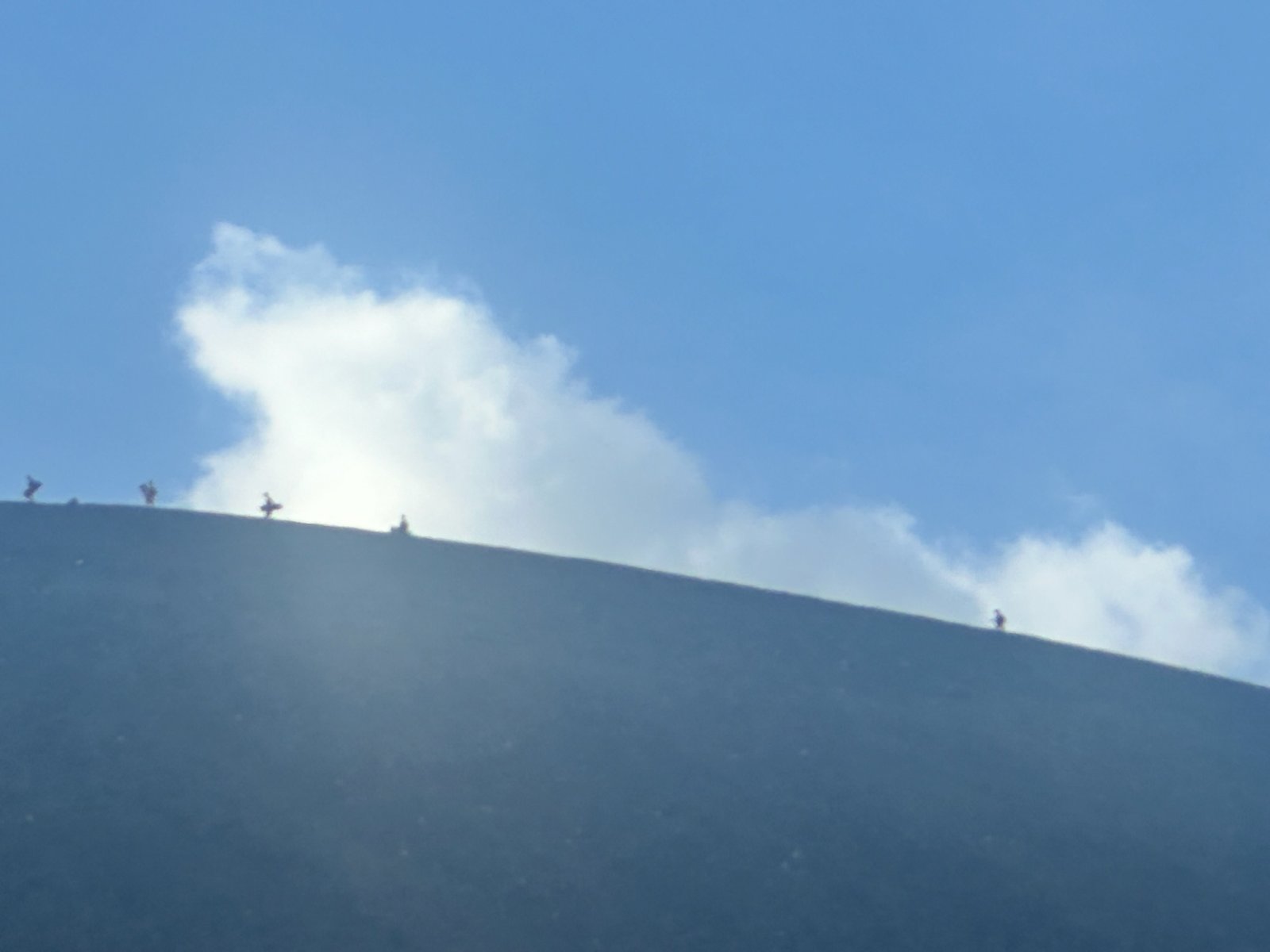 Small figures walking the ash ridge of a volcano against blue sky