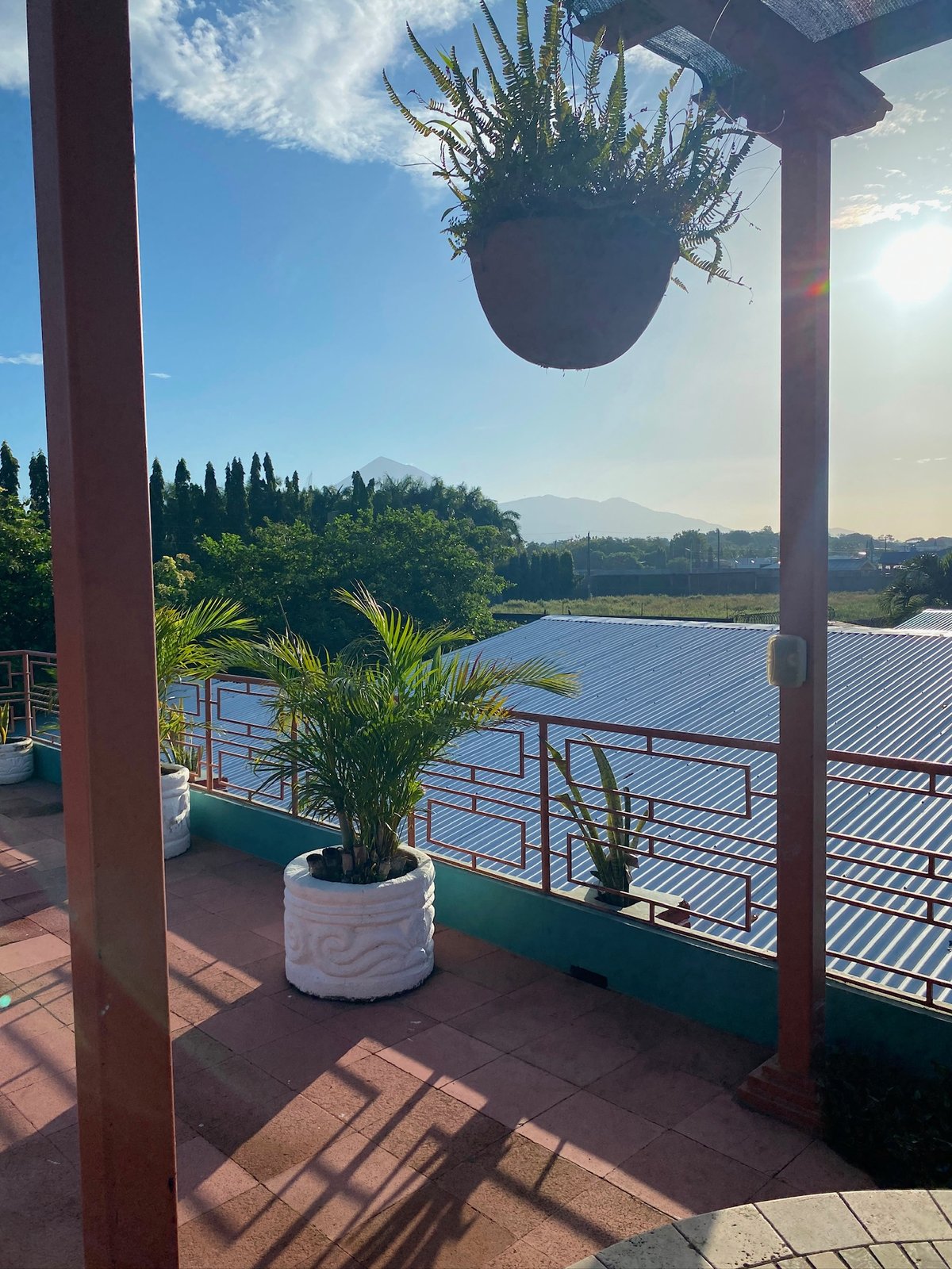 View from a compound balcony over a metal roof toward a volcano under a clear sky
