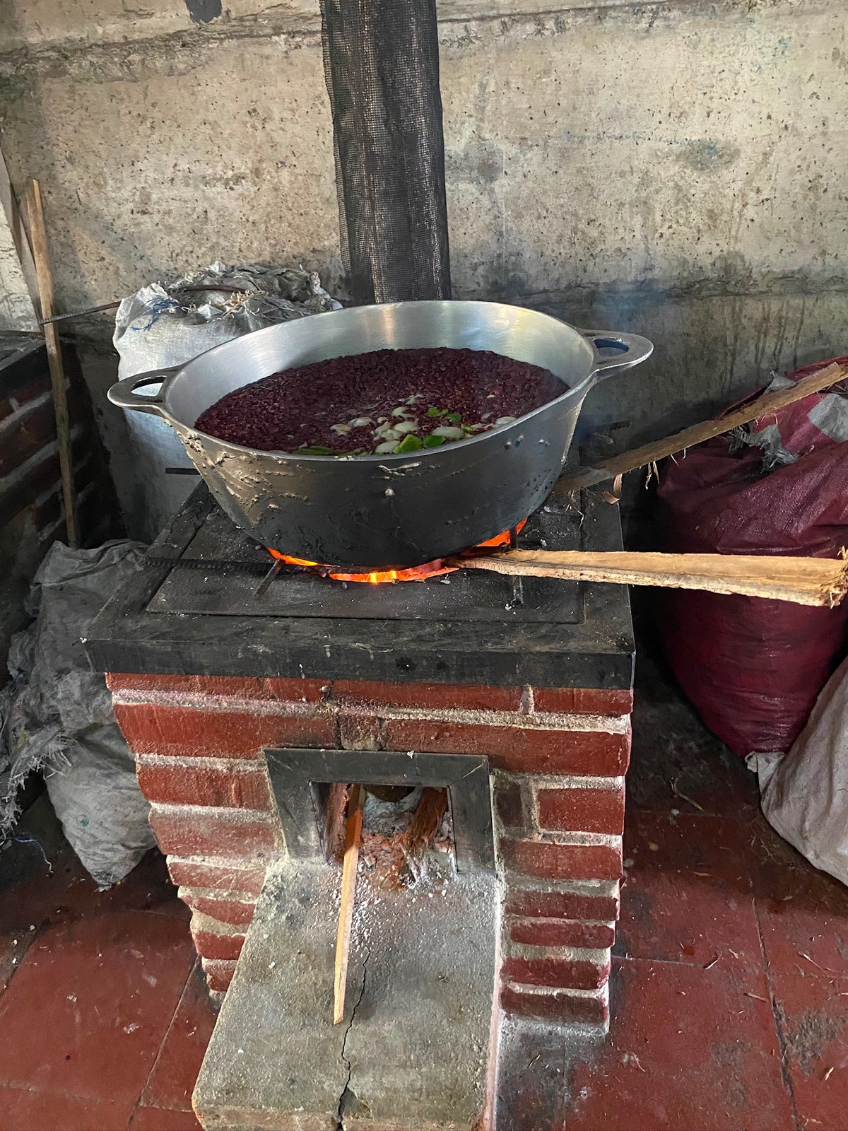 Large pot of red beans with onion cooking over a wood-fired brick stove