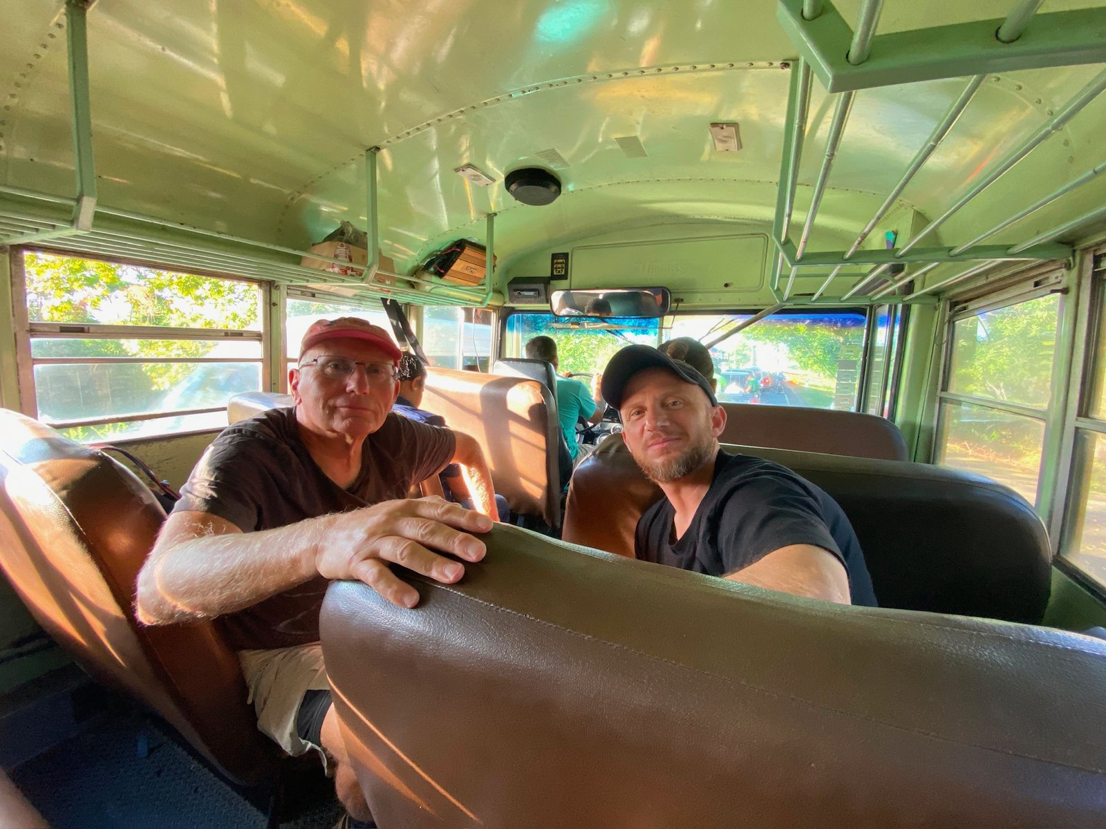Two team members seated inside a green-painted bus looking at the camera