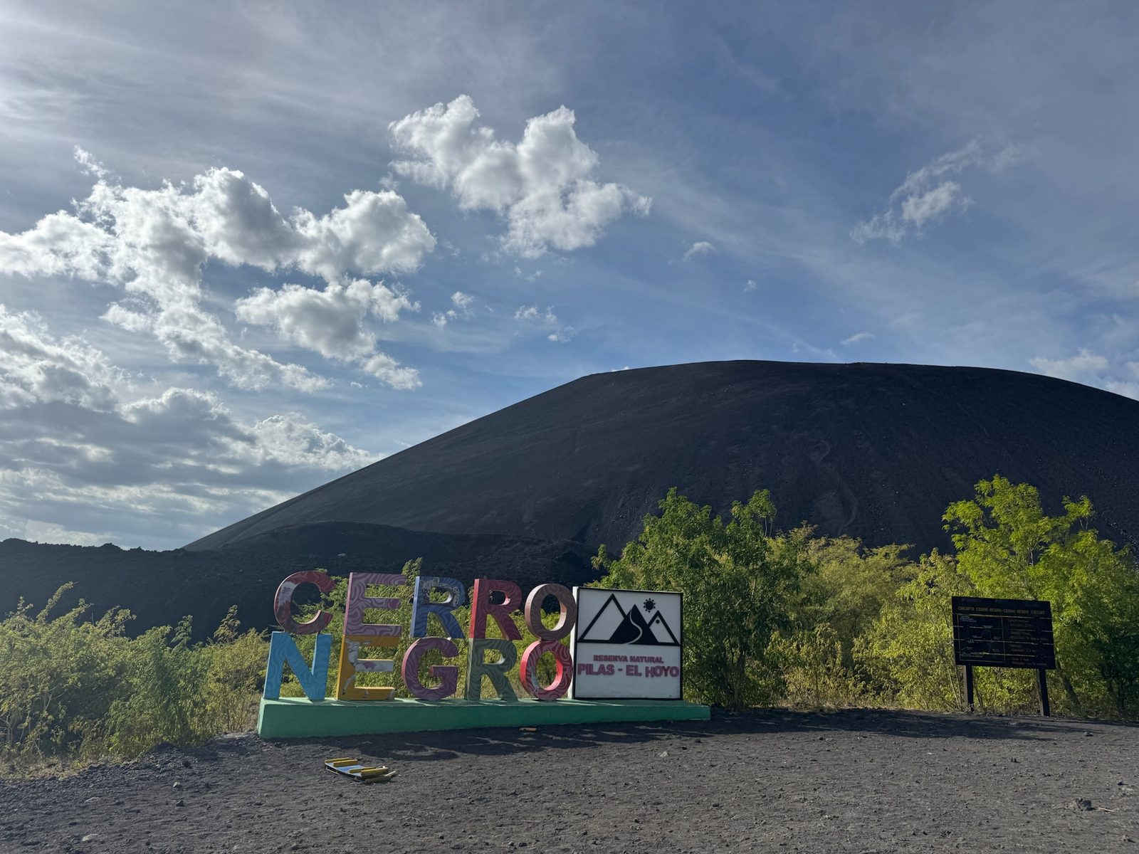 Dark Cerro Negro cinder cone under blue sky with colorful CERRO NEGRO letters in the foreground