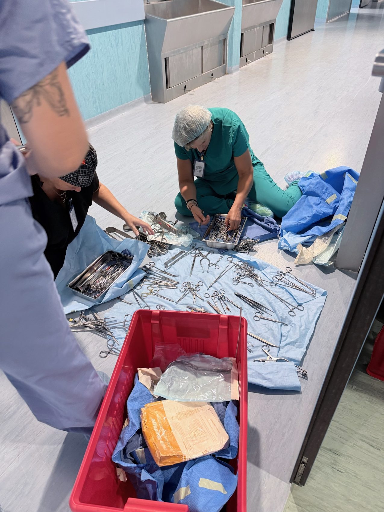 Team sitting on a hospital hallway floor cleaning instruments on blue wrap