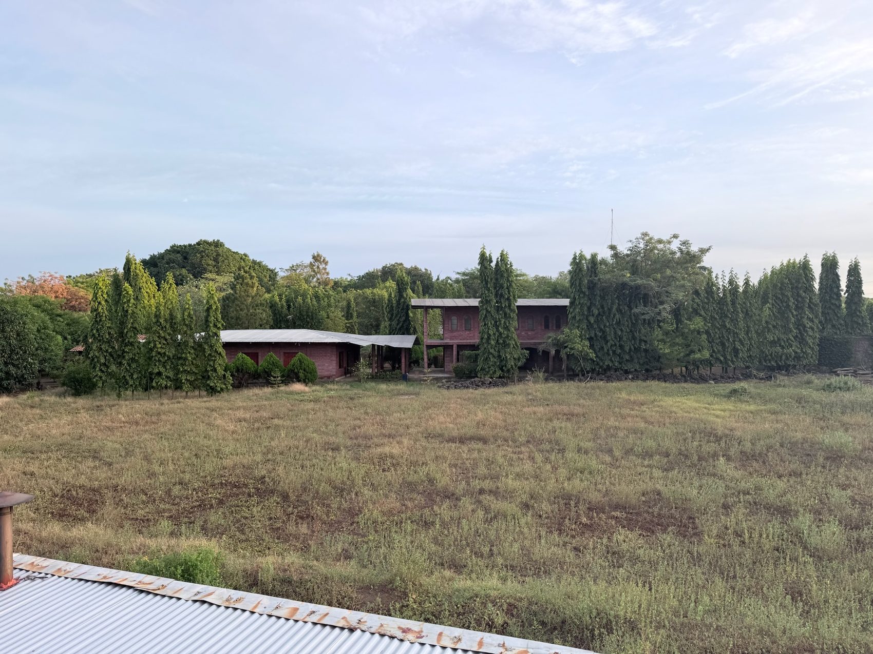 View from a balcony over dry grass and terracotta roofs at the compound