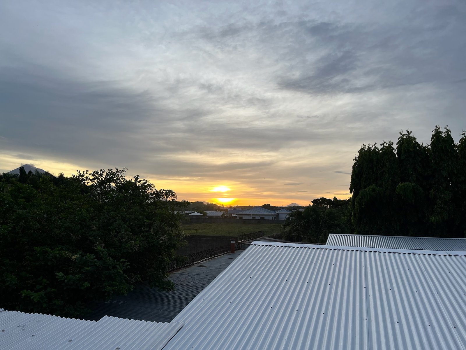 Sunset over rooftops and trees with a volcanic cone on the horizon