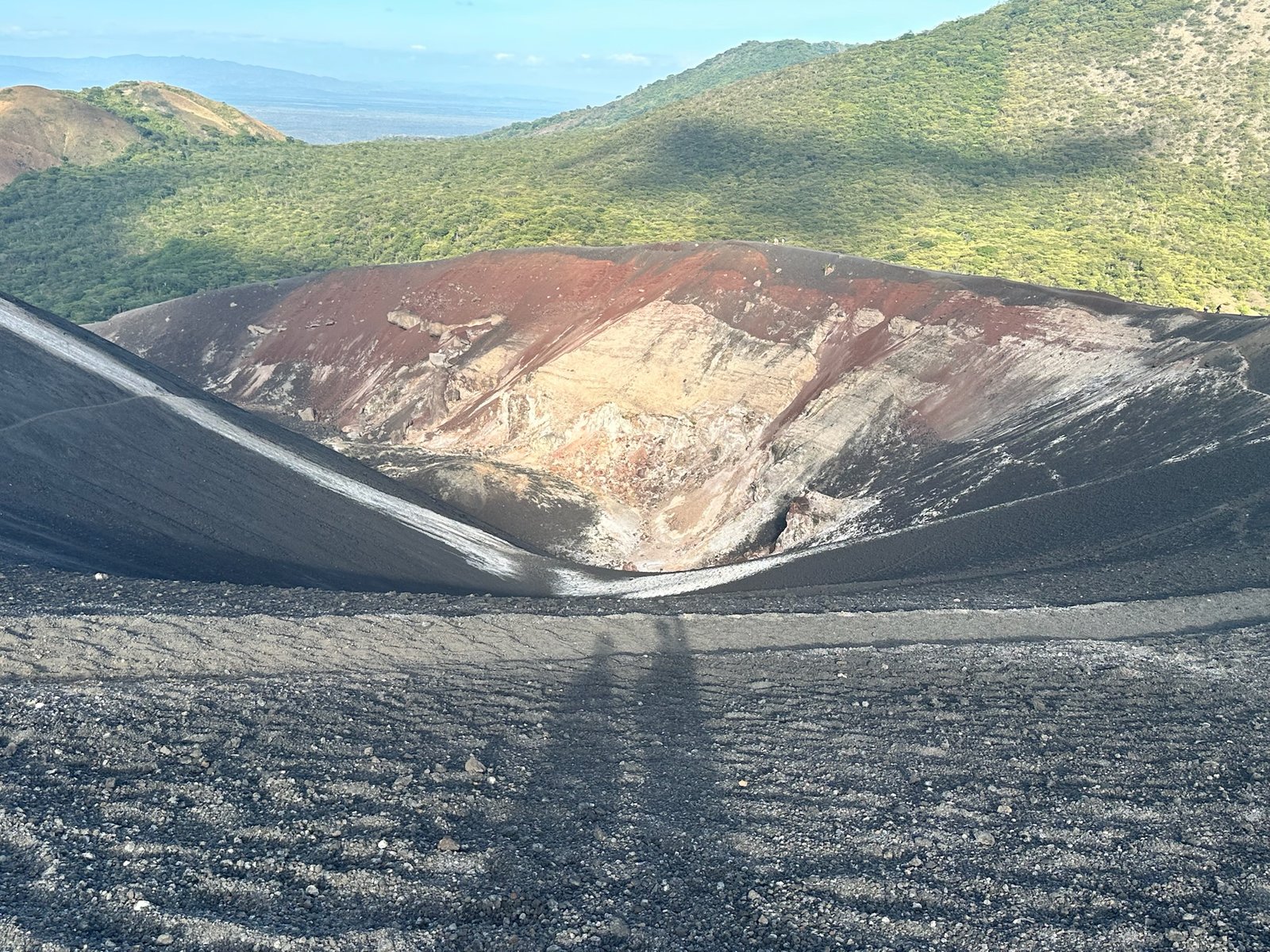 Looking down into a volcanic crater from the rim, ash path and green far wall