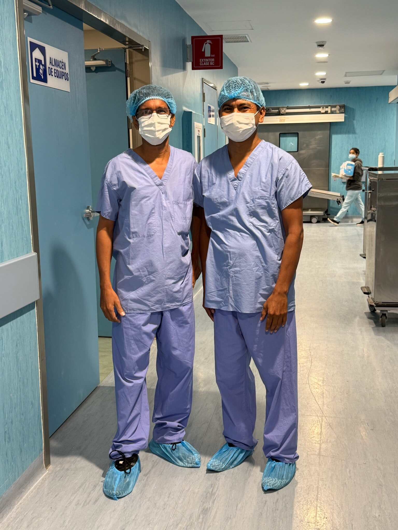 Two of the team's translators wearing surgical scrubs, caps, and masks in a hospital corridor