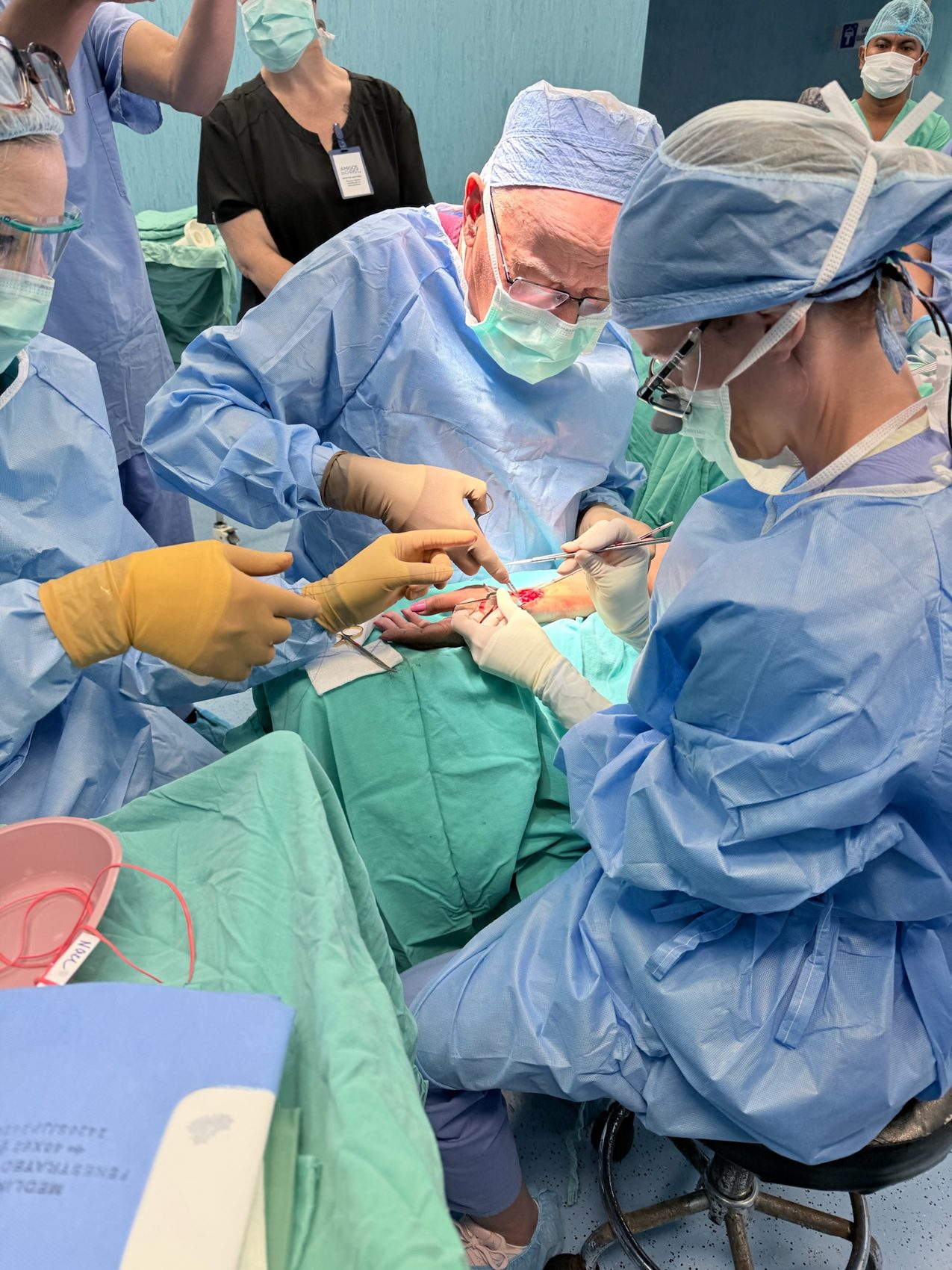 Surgeons with loupes creating an arteriovenous fistula at the wrist; patient face not shown