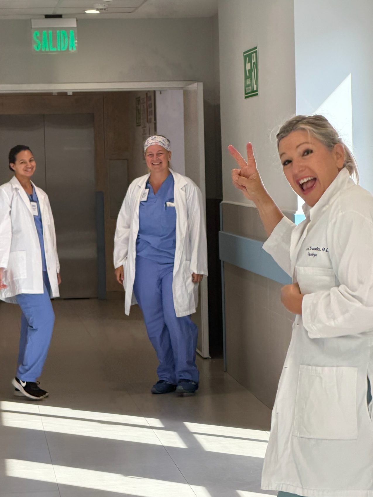 Team members in lab coats in a hospital corridor under a green SALIDA sign