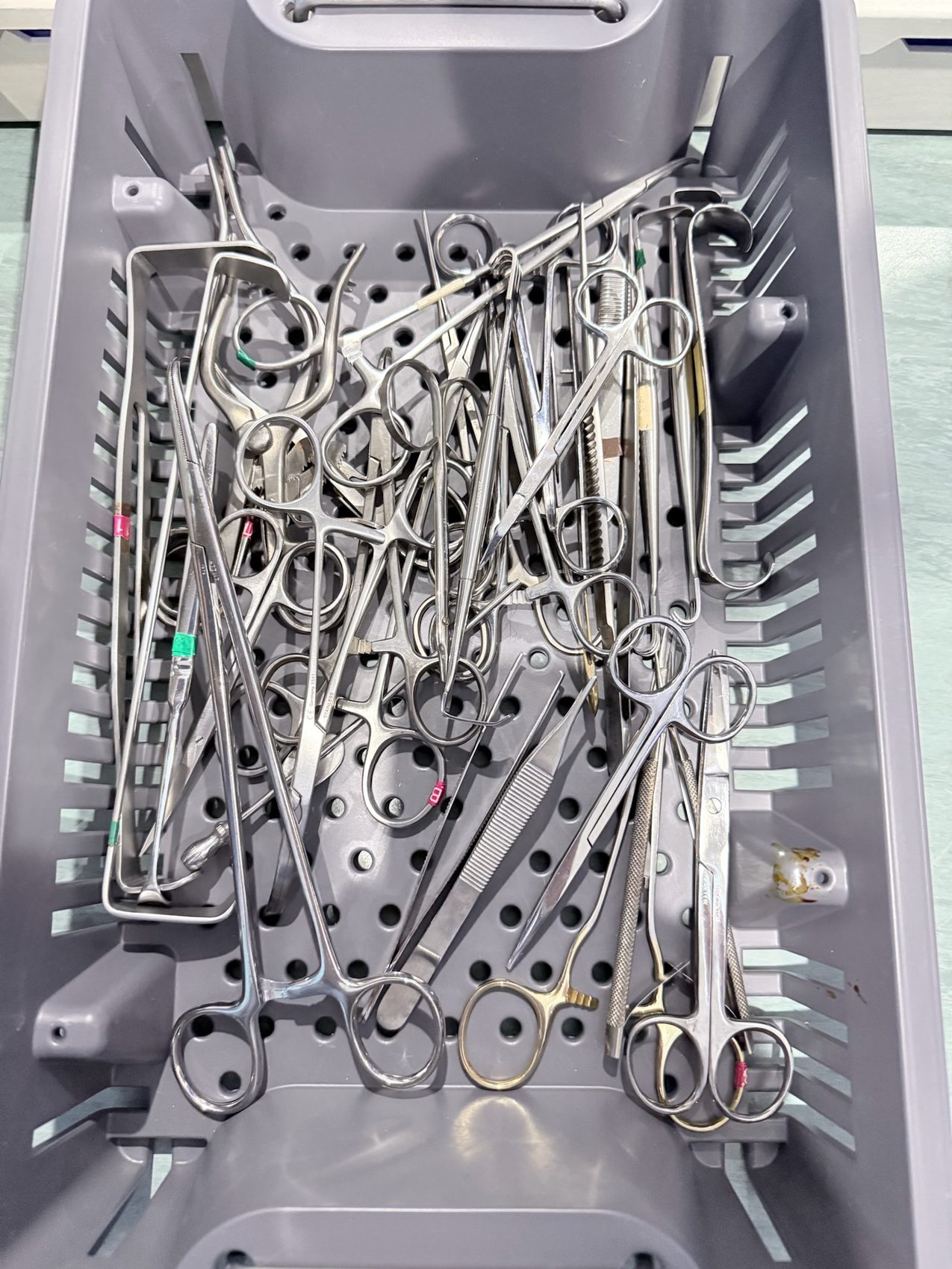 Perforated gray tray filled with clamps, scissors, and hemostats