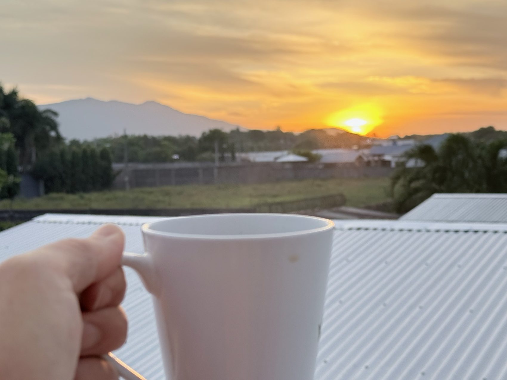 A coffee mug held against a sunrise over Chinandega hills