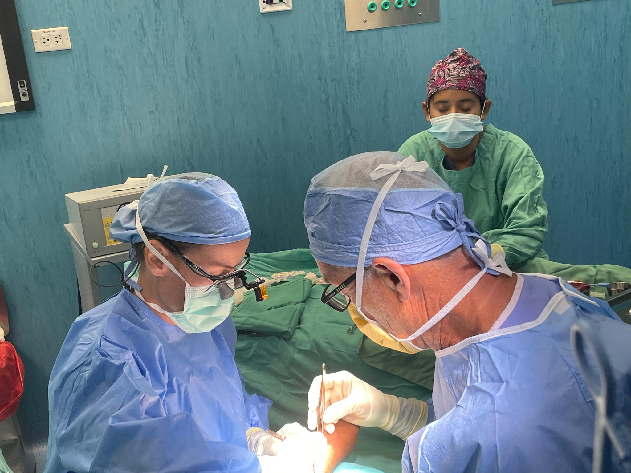 Two surgeons in loupes operating at the table, a third team member behind them