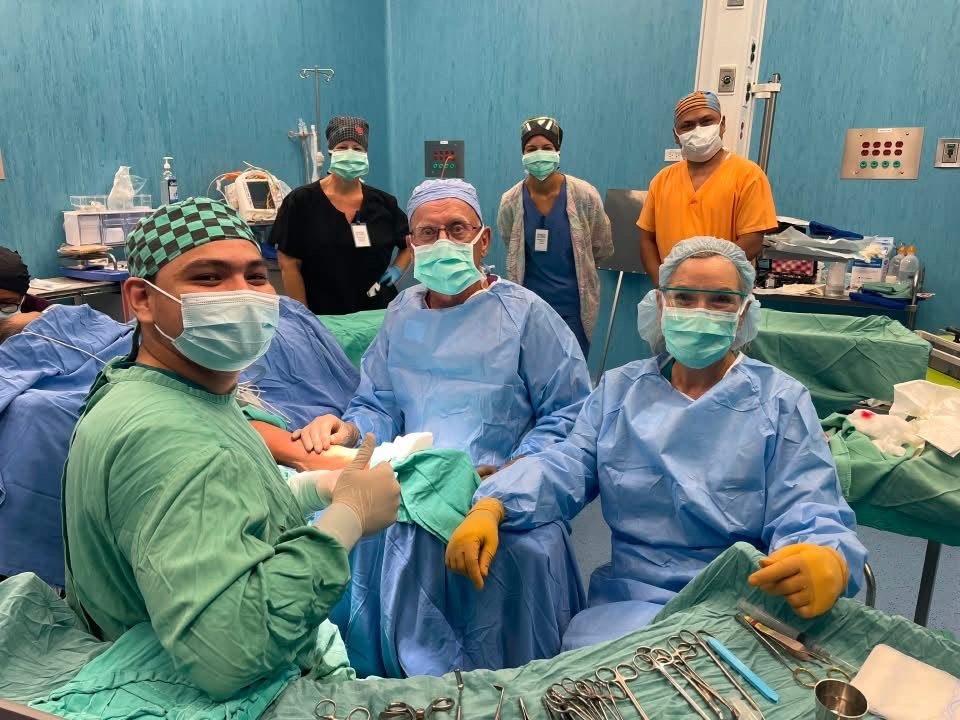 Six team members in scrubs posing in the operating room; patient draped, face not shown
