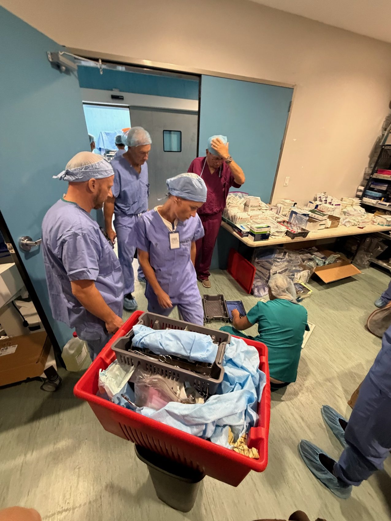 Team around a red crate of drapes and trays before the next operating room