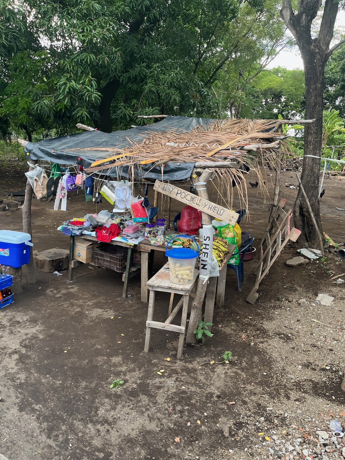 Roadside stall with a hand-painted sign HAY POCICLE Y HIELO, bananas, and corn