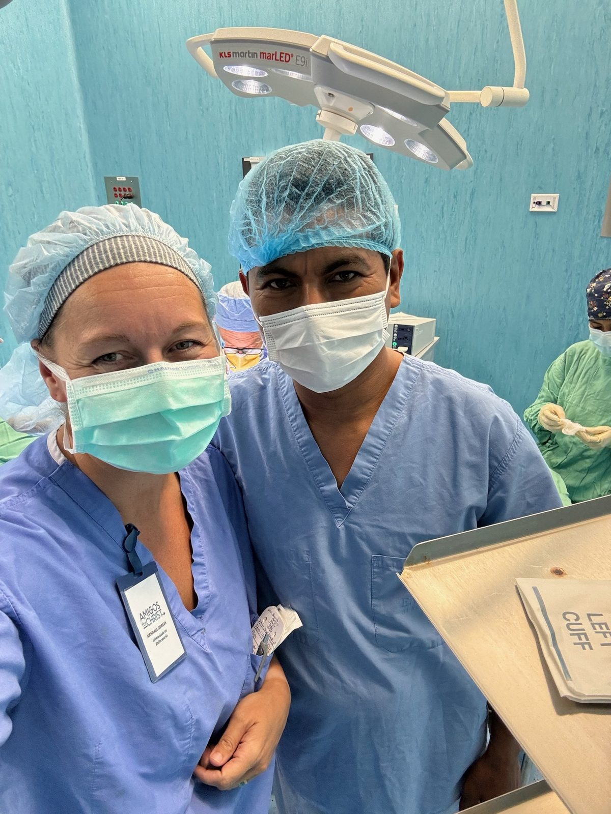 Kendall Clare Adrian, RN BSN in blue scrubs, cap, and mask smiling in the operating room