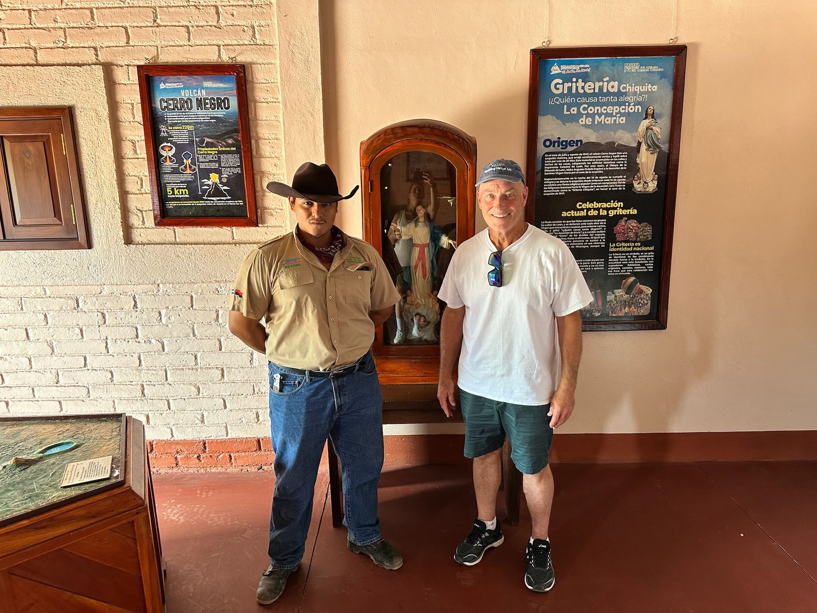 Two visitors beside a wooden shrine and Cerro Negro and Griteria posters
