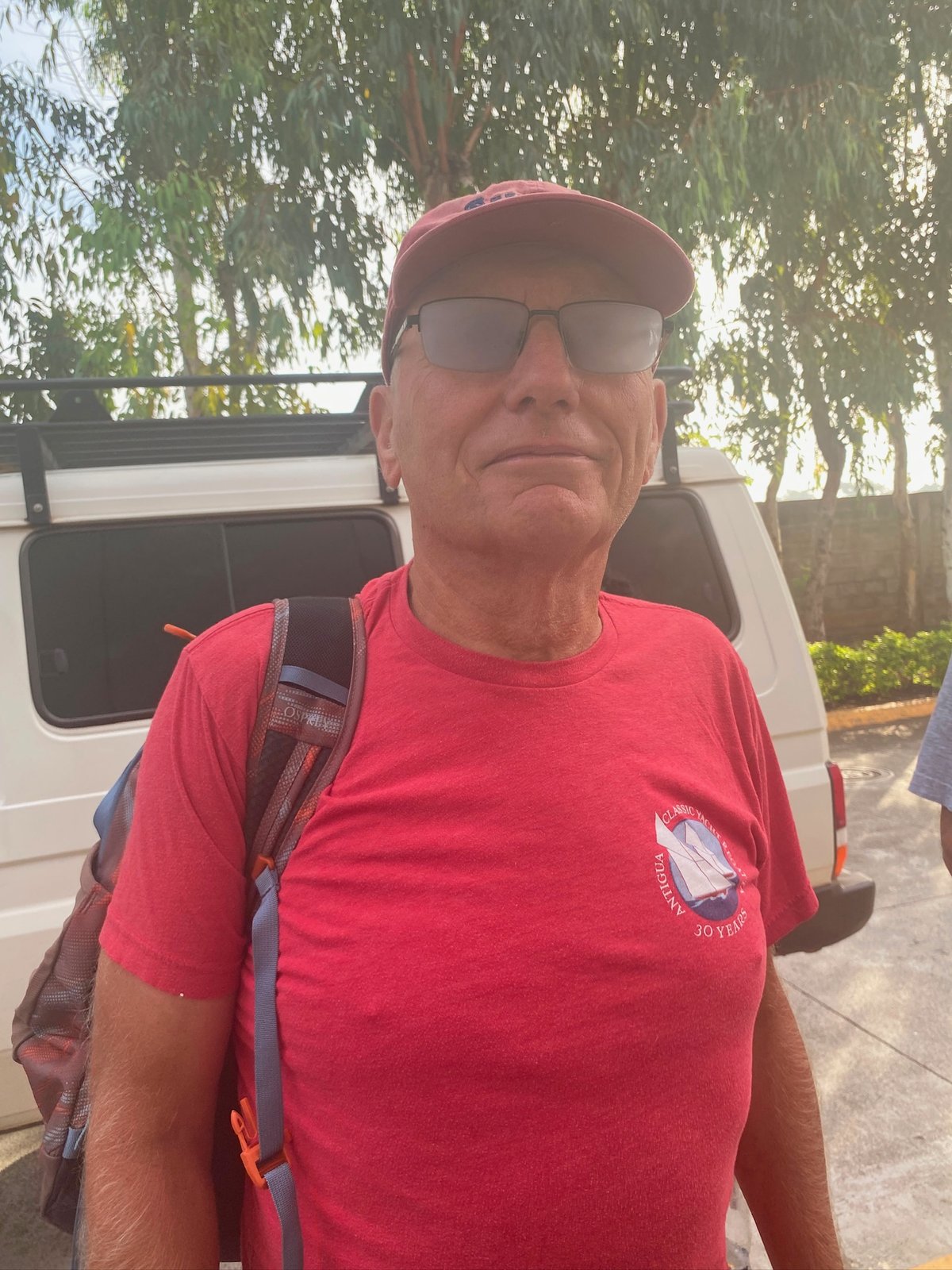 Nicholas Peter Maxwell in a red shirt and red cap standing outdoors near a vehicle