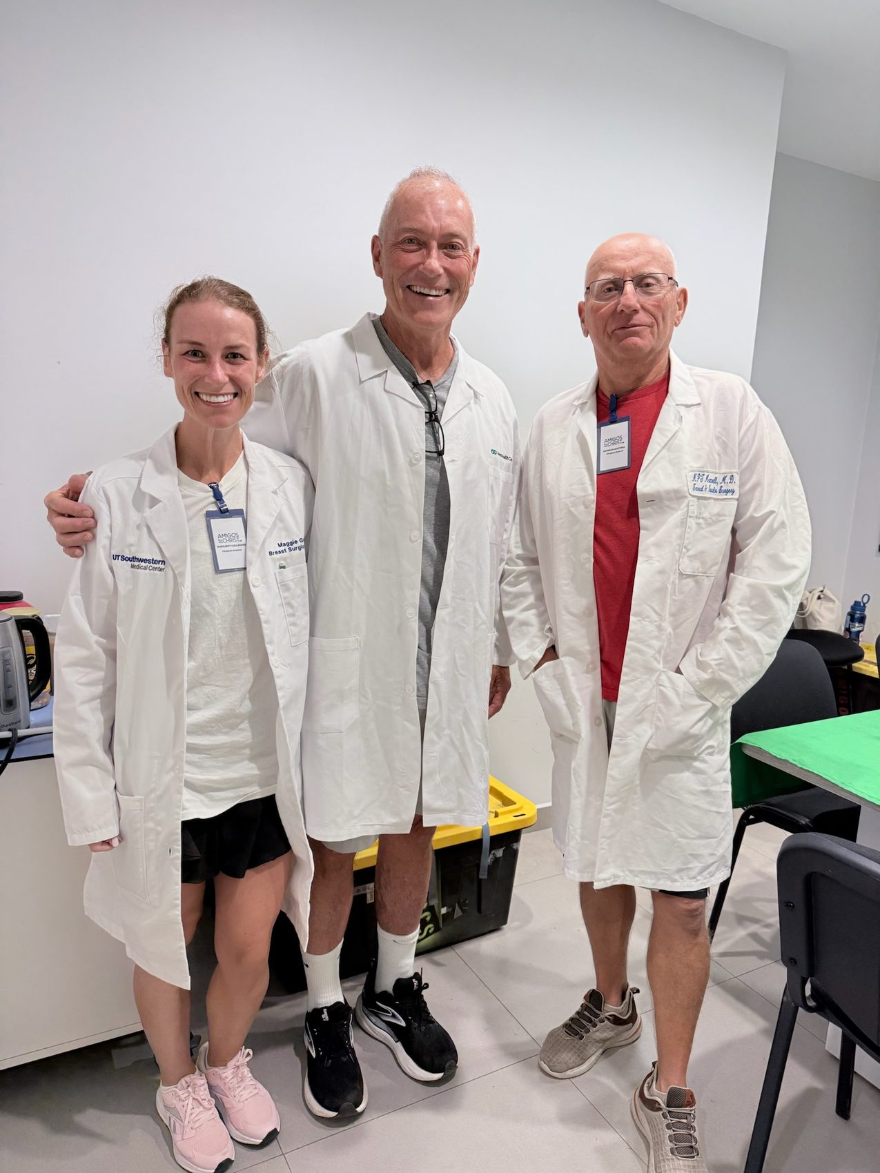 Three visiting clinicians in white coats standing in a hospital workroom