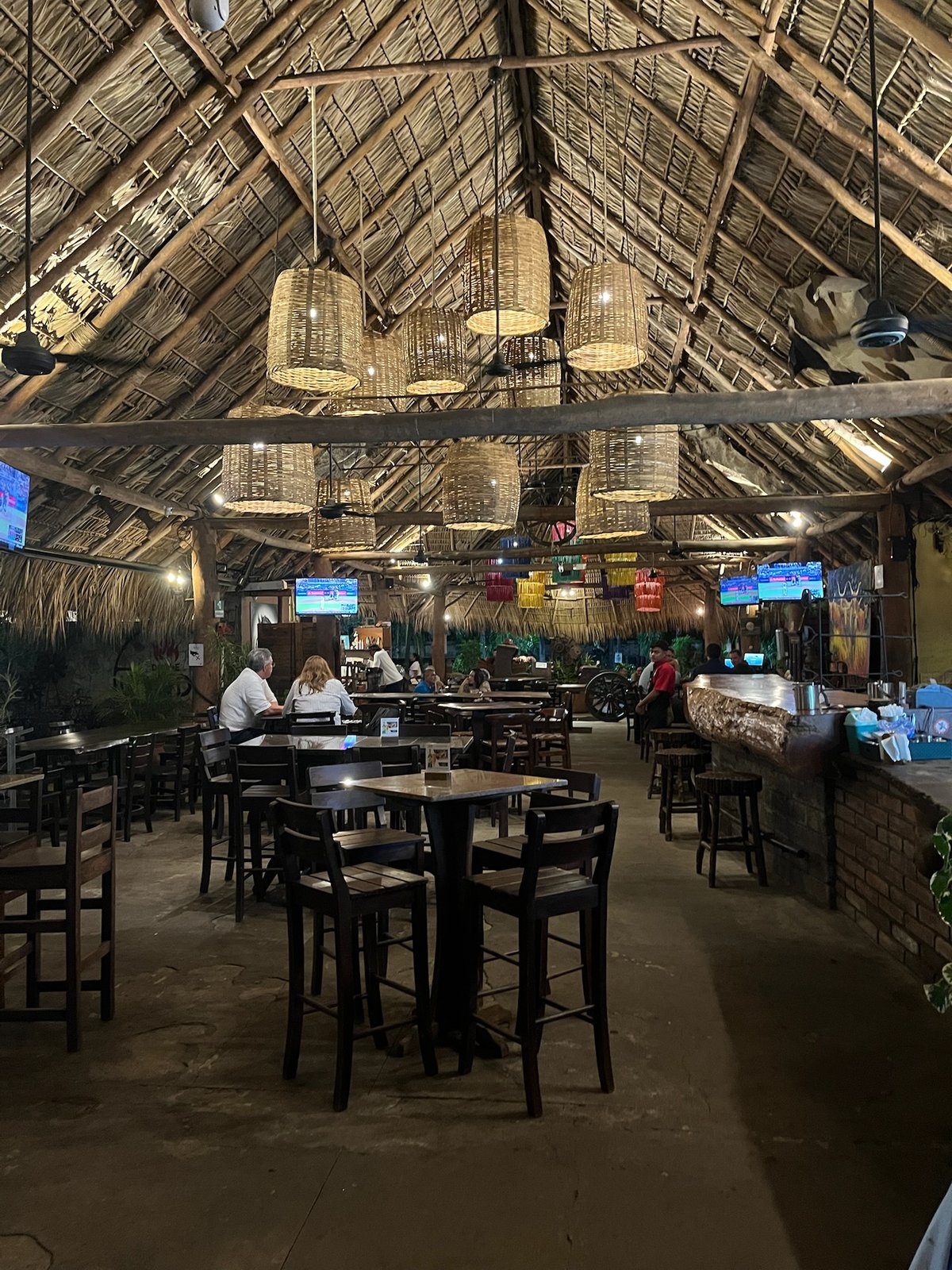 Interior of a thatched-roof restaurant with woven pendant lamps and wooden tables