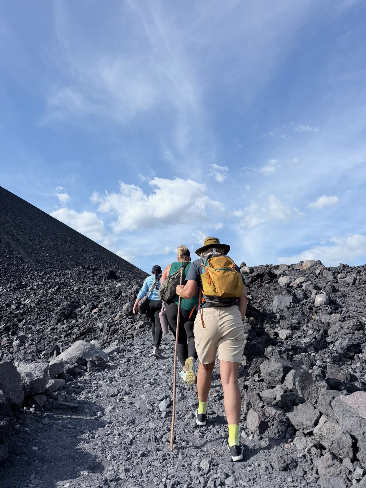 Three hikers climbing a steep volcanic ash trail, seen from behind