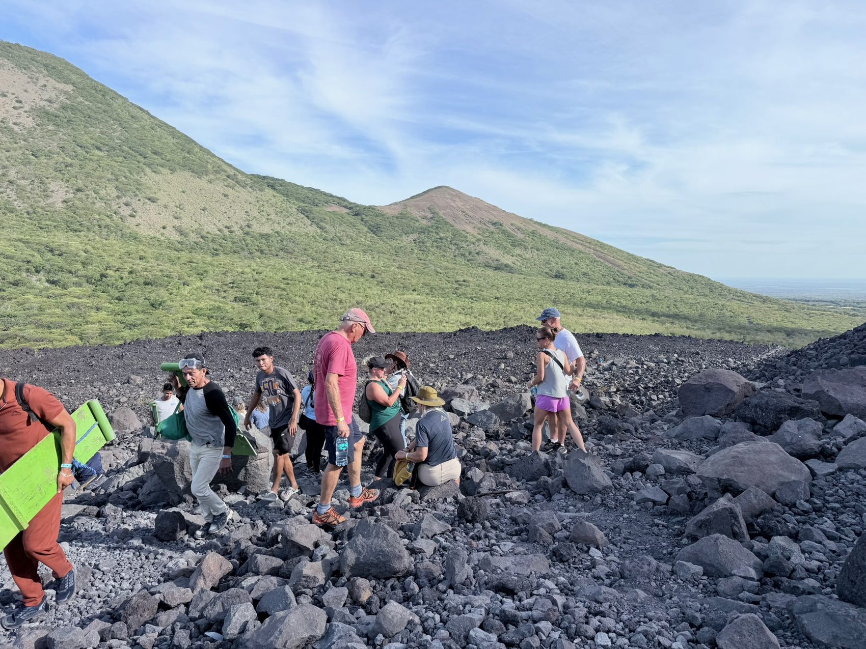 Team hiking a volcanic field carrying volcano boards, green cones behind