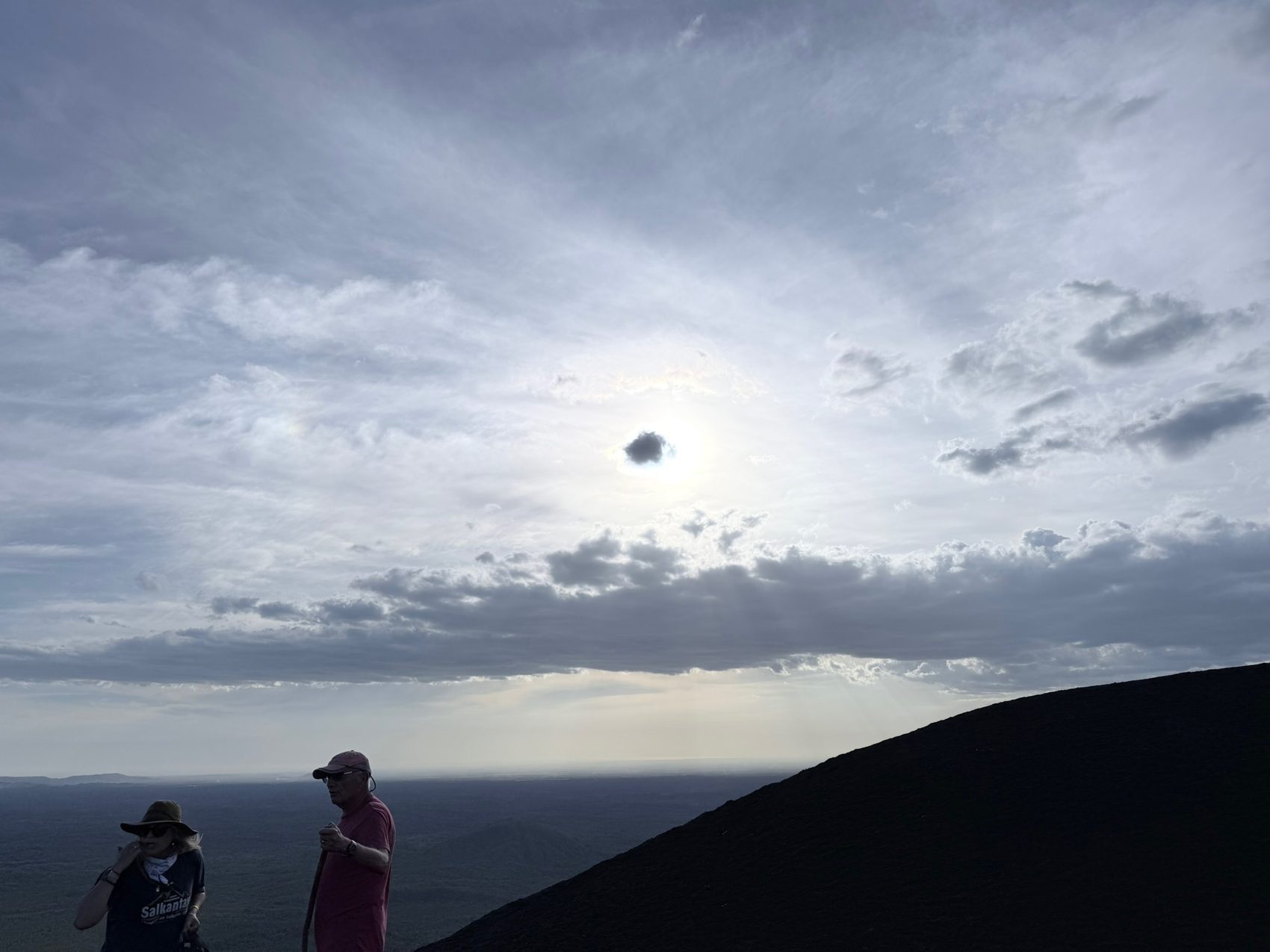 Two team members on a cinder slope watching the sun over a wide plain
