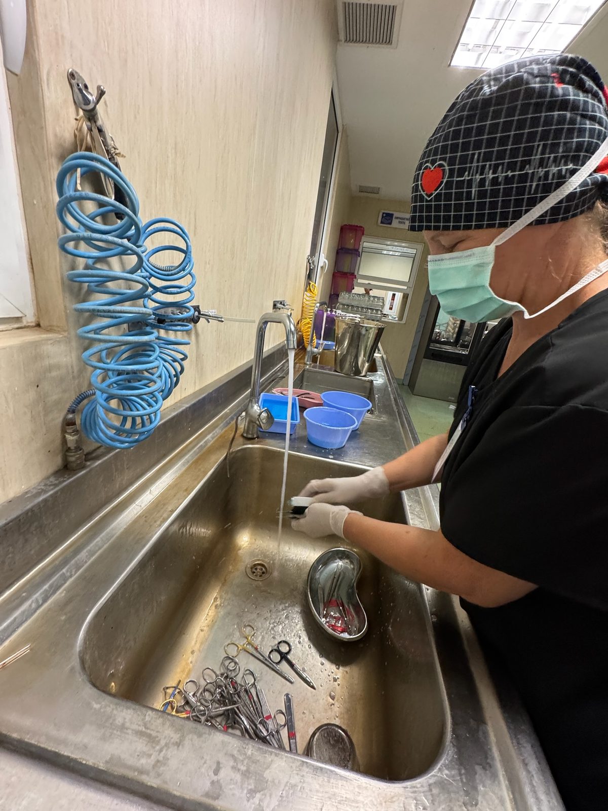Team member in a mask washing surgical instruments in a stainless steel sink